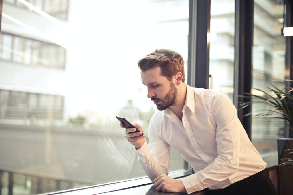 un-homme-en-chemise-blanche-tenant-un-telephone-pres-de-la-fenetre